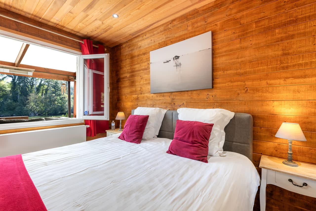 Groot bed in de houten slaapkamer, rode kussens en schilderij