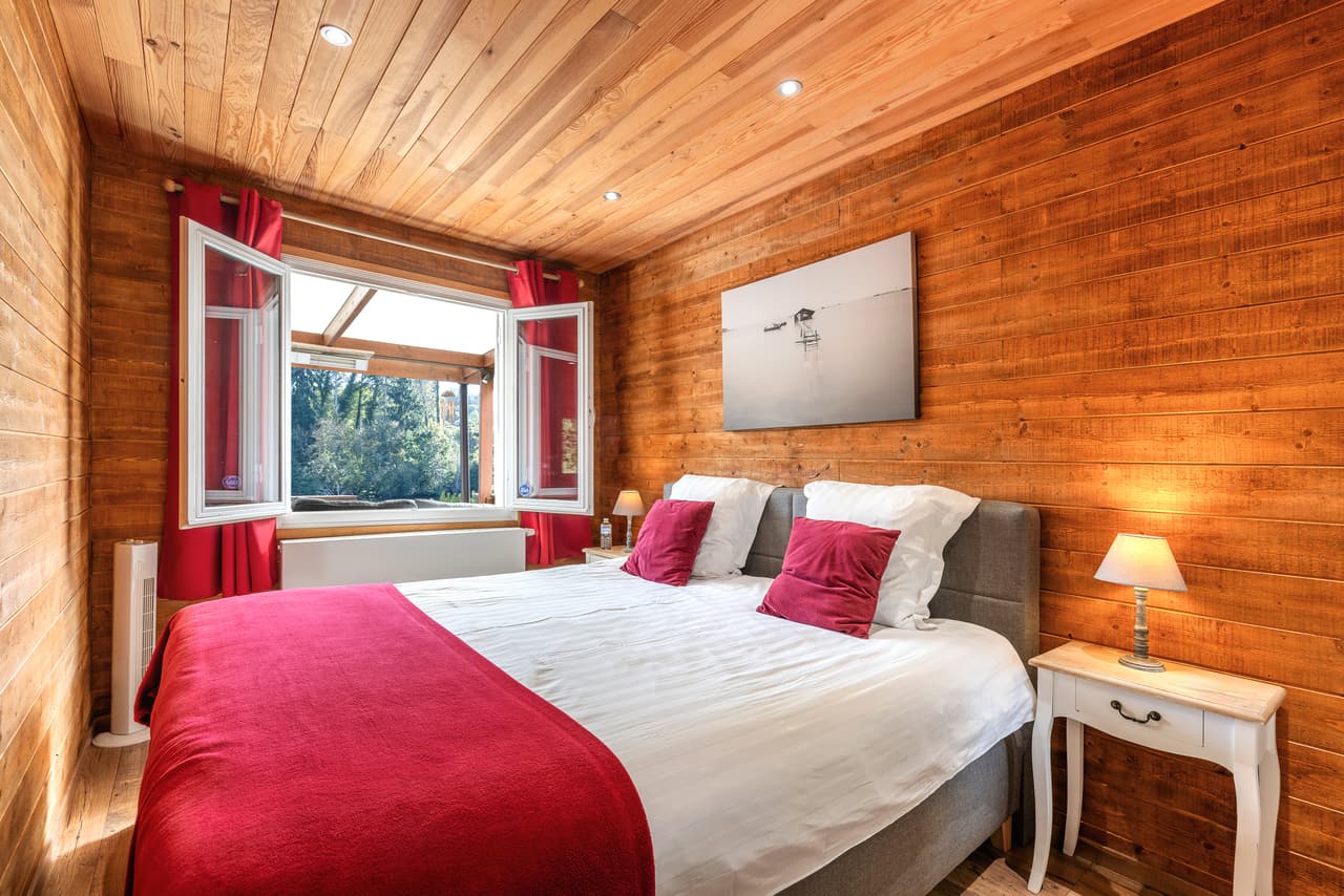Houten slaapkamer met rode sprei en open ramen