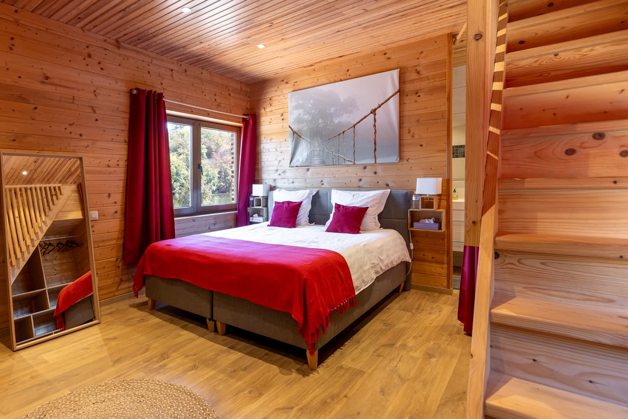 Houten slaapkamer met rode sprei, aan de voet van de trap