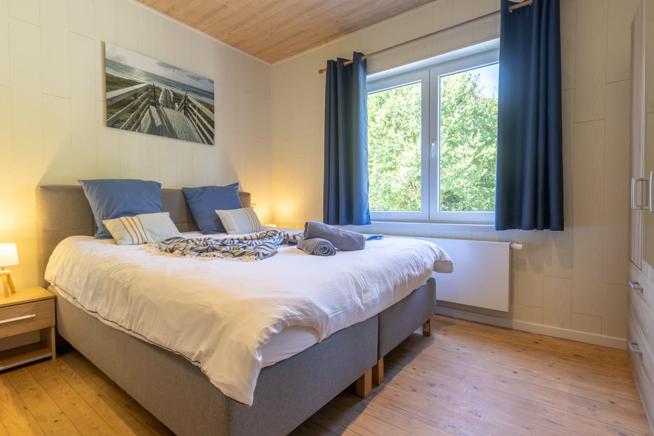 Slaapkamer met blauwe gordijnen, groot bed en raam op het groen